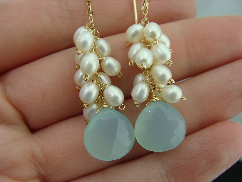 May include: A pair of dangle earrings with a light blue gemstone and a cluster of white pearls hanging from a gold wire.