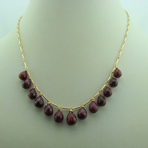May include: A gold chain necklace with teardrop-shaped red gemstones.