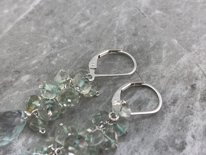 May include: A pair of silver dangle earrings featuring light blue gemstone beads. The earrings have a teardrop-shaped gemstone at the bottom.