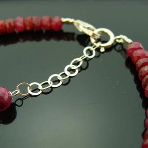 May include: A close-up of a red gemstone bracelet with a silver clasp. The bracelet is made of small, round beads and has a delicate chain.