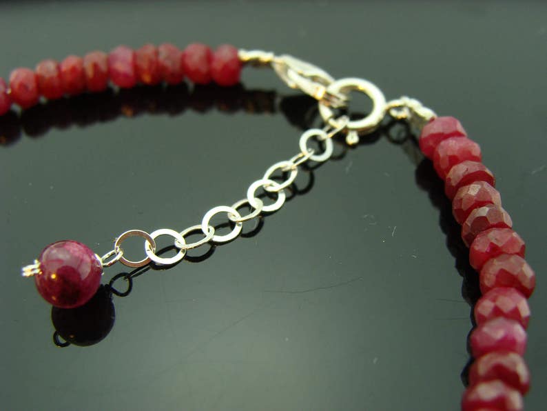 May include: A close-up of a red gemstone bracelet with a silver clasp. The bracelet is made of small, round beads and has a delicate chain.