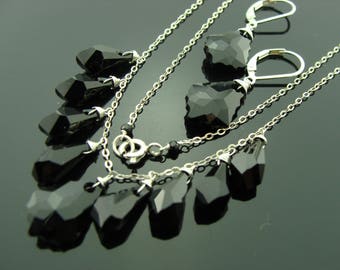 Puede incluir: Un conjunto de collar y pendientes de plata con colgantes de cristal negro en forma de lágrima y cuadrada. El collar tiene múltiples cadenas y los pendientes tienen un diseño colgante.