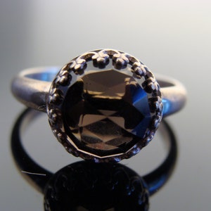 Puede incluir: Un anillo de plata con una piedra preciosa marr&oacute;n engastada en un engaste de plata decorativo. El anillo tiene un dise&ntilde;o delicado y ornamentado.