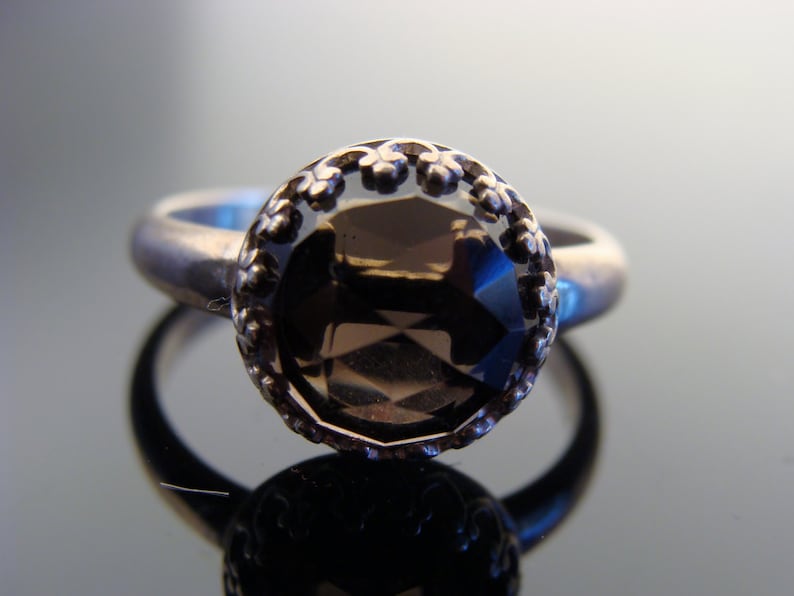 Puede incluir: Un anillo de plata con una piedra preciosa marr&oacute;n engastada en un engaste de plata decorativo. El anillo tiene un dise&ntilde;o delicado y ornamentado.