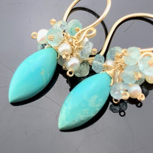 Op de afbeelding: Gouden oorhangers met turquoise druppelstenen en een cluster van aquamarijn en witte parels.