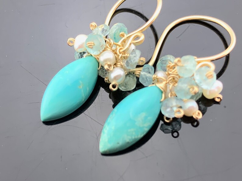 Op de afbeelding: Gouden oorhangers met turquoise druppelstenen en een cluster van aquamarijn en witte parels.