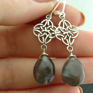 May include: Silver Celtic knot earrings with dark gray teardrop-shaped gemstone pendants.