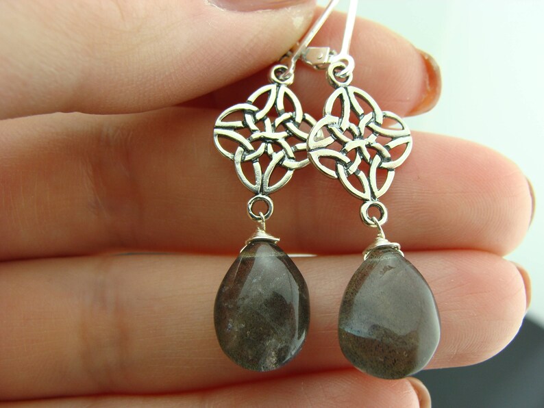 May include: Silver Celtic knot earrings with dark gray teardrop-shaped gemstone pendants.