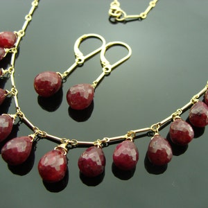 May include: A gold necklace with a delicate chain and dangling ruby red gemstone drops. Matching ruby red gemstone earrings with gold posts.