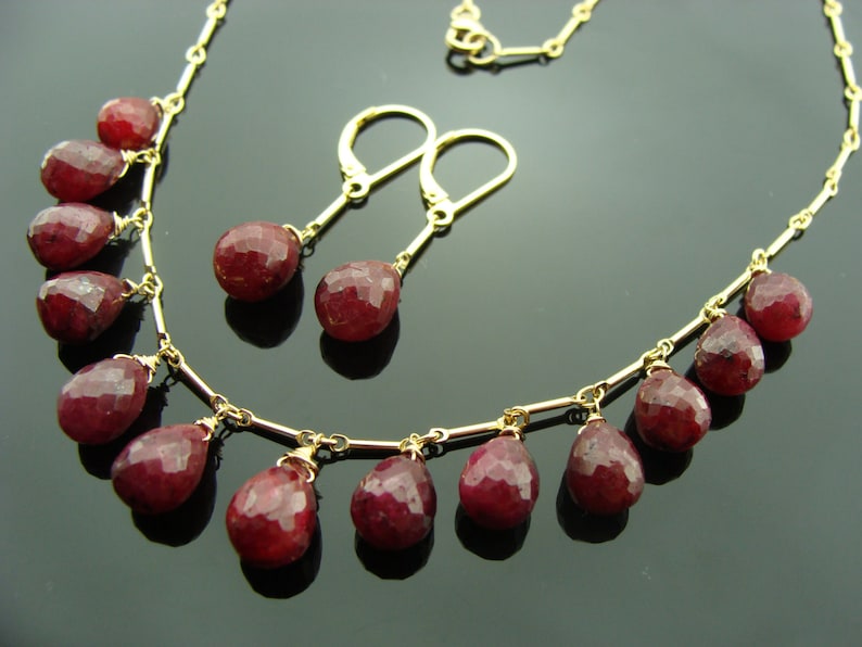 May include: A gold necklace with a delicate chain and dangling ruby red gemstone drops. Matching ruby red gemstone earrings with gold posts.