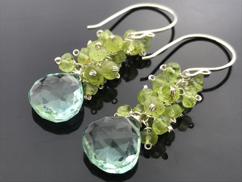 Op de afbeelding: Zilveren oorhangers met een traanvormige lichtgroene edelsteen en een cluster van kleinere lichtgroene edelstenen.