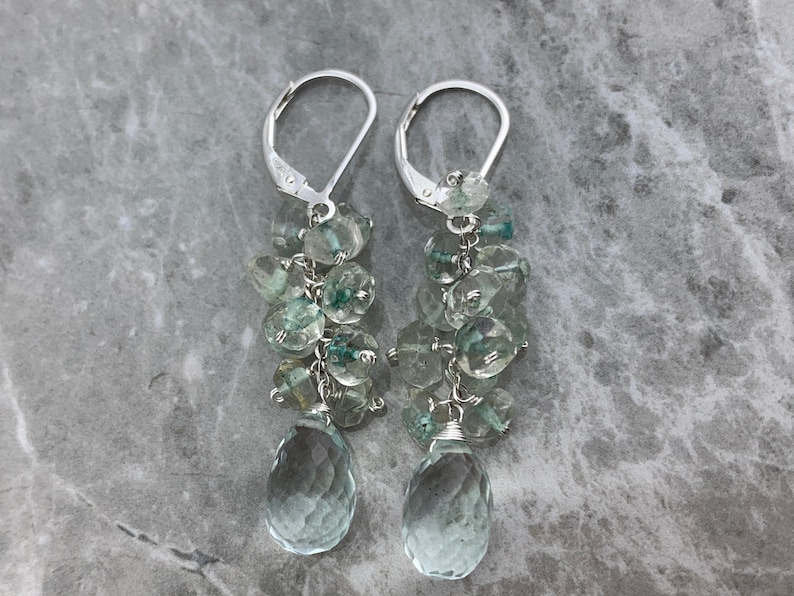 May include: A pair of silver dangle earrings featuring a cluster of light blue and green gemstone beads, with a larger teardrop-shaped gemstone at the bottom.