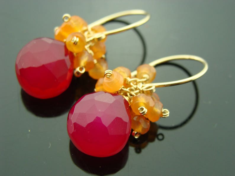 May include: Gold earrings with a teardrop-shaped pink chalcedony gemstone and orange carnelian beads.