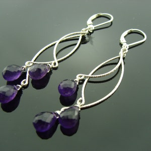 May include: A pair of silver dangle earrings with three amethyst gemstones on each earring. The earrings have a delicate, interwoven design.