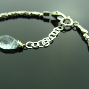May include: A silver bracelet with a light blue gemstone pendant. The bracelet is made of small, faceted beads and has a lobster claw clasp.