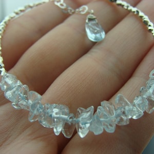May include: A silver bracelet with a delicate chain and a light blue gemstone pendant. The bracelet is adorned with a row of light blue gemstone chips.