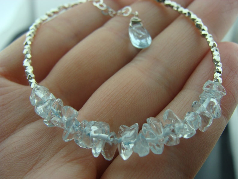 May include: A silver bracelet with a delicate chain and a light blue gemstone pendant. The bracelet is adorned with a row of light blue gemstone chips.
