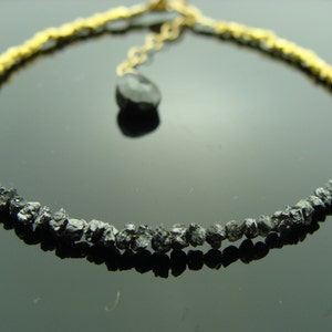 May include: A black diamond bracelet with gold beads. The bracelet is made of rough, uncut black diamonds and gold beads. The bracelet is accented with a single black diamond pendant.