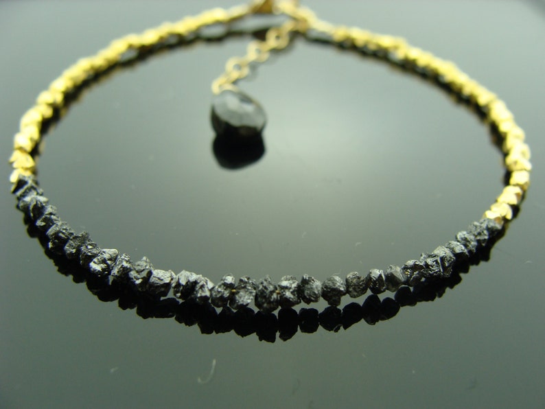 May include: A black diamond bracelet with gold beads. The bracelet is made of rough, uncut black diamonds and gold beads. The bracelet is accented with a single black diamond pendant.