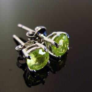 May include: A pair of silver earrings with green peridot gemstones. The earrings have a simple design and are perfect for everyday wear.