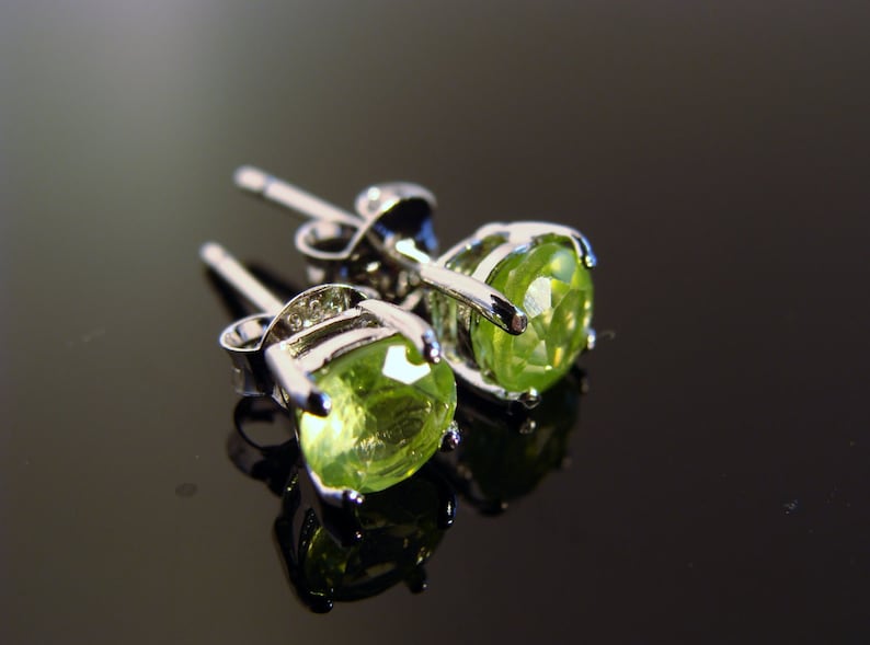 May include: A pair of silver earrings with green peridot gemstones. The earrings have a simple design and are perfect for everyday wear.