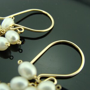 May include: A pair of gold dangle earrings with white pearl clusters. The earrings have a simple, elegant design.