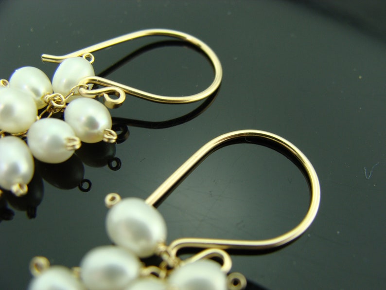 May include: A pair of gold dangle earrings with white pearl clusters. The earrings have a simple, elegant design.
