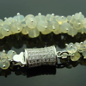 May include: A silver bracelet with a clasp made of small white stones. The bracelet is made of white opal beads.
