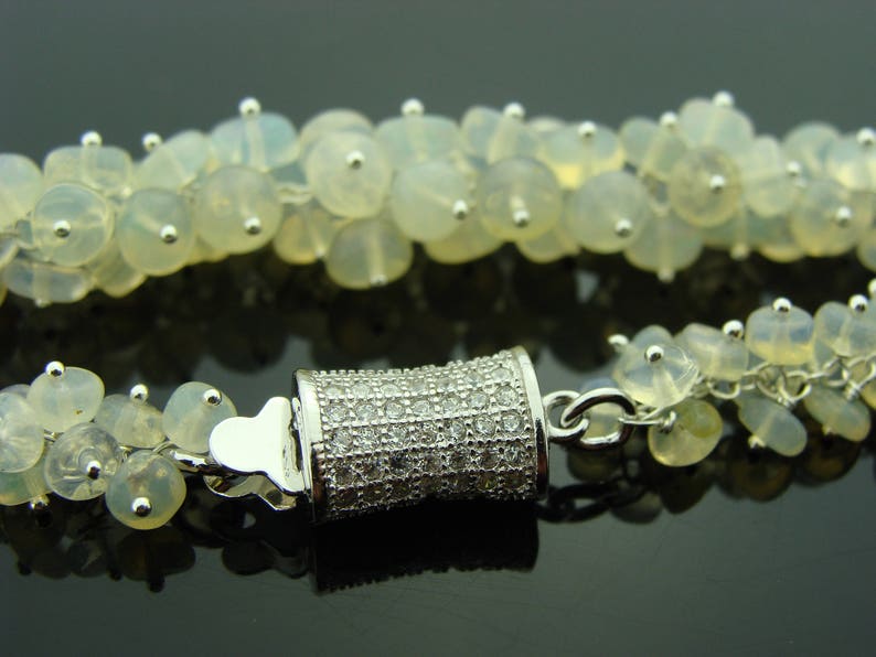 May include: A silver bracelet with a clasp made of small white stones. The bracelet is made of white opal beads.