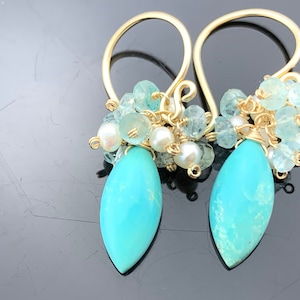 Op de afbeelding: Gouden oorbellen met een turquoise traanvormige steen en een cluster van aquamarijn en parels.