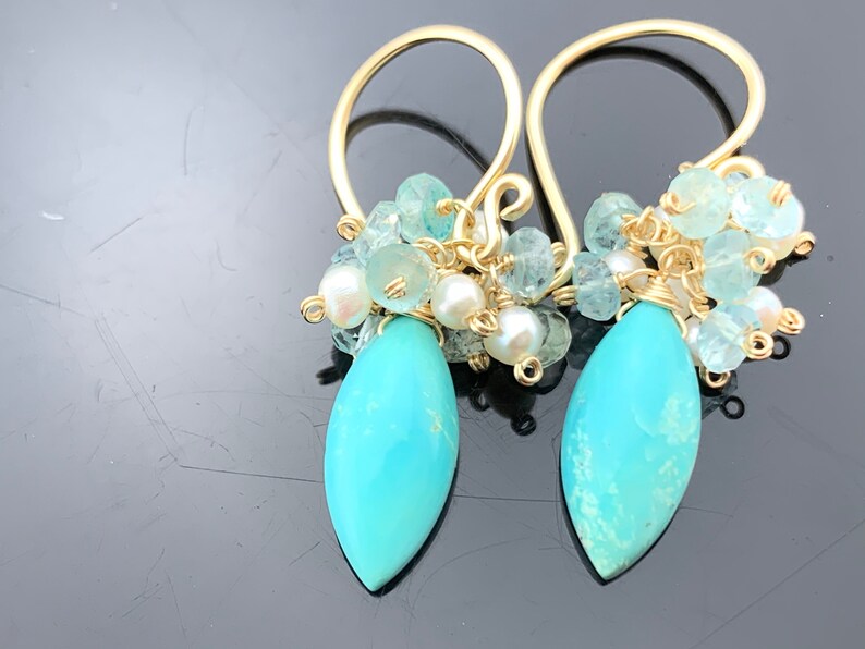 Op de afbeelding: Gouden oorbellen met een turquoise traanvormige steen en een cluster van aquamarijn en parels.