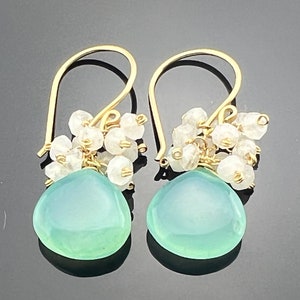 May include: Gold dangle earrings with a light blue teardrop-shaped gemstone and a cluster of white beads.