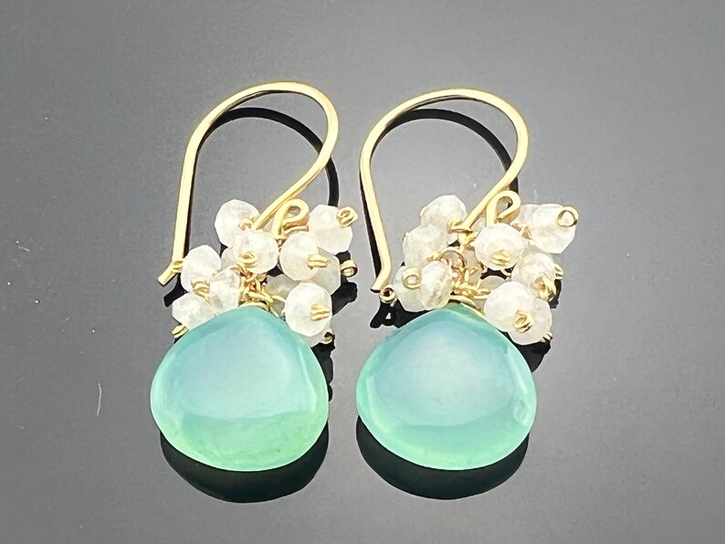 May include: Gold dangle earrings with a light blue teardrop-shaped gemstone and a cluster of white beads.