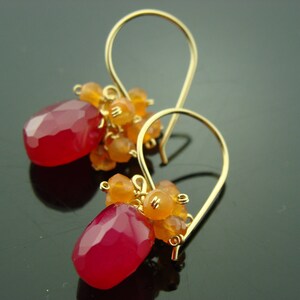 May include: Gold earrings with pink and orange gemstone drops. The earrings are made with a delicate gold wire and feature a cluster of small orange gemstones at the top of each drop.