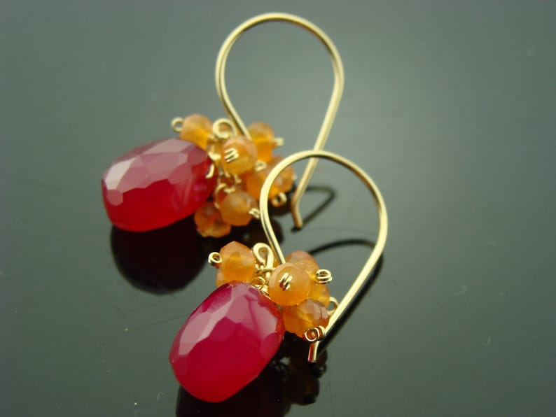 May include: Gold earrings with pink and orange gemstone drops. The earrings are made with a delicate gold wire and feature a cluster of small orange gemstones at the top of each drop.