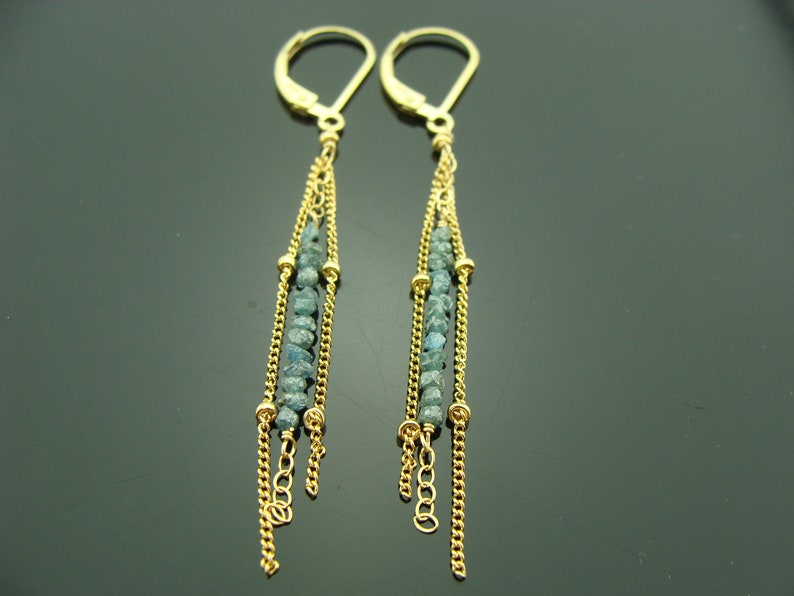 Puede incluir: Pendientes de oro con un dise&ntilde;o largo y colgante. Los pendientes presentan m&uacute;ltiples hebras de cadena con peque&ntilde;as cuentas de piedras preciosas azules.