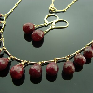 May include: A gold necklace with a delicate chain and dangling ruby red gemstone drops. Matching ruby red gemstone earrings with gold posts and hooks.