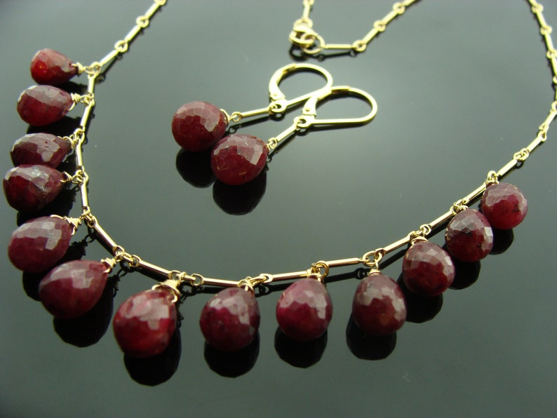 May include: A gold necklace with a delicate chain and dangling ruby red gemstone drops. Matching ruby red gemstone earrings with gold posts and hooks.