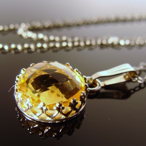 May include: A silver chain necklace with a pendant featuring a large, faceted, yellow gemstone set in a silver filigree frame.