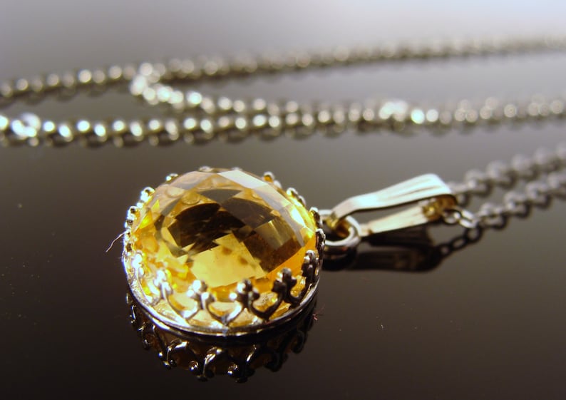 May include: A silver chain necklace with a pendant featuring a large, faceted, yellow gemstone set in a silver filigree frame.