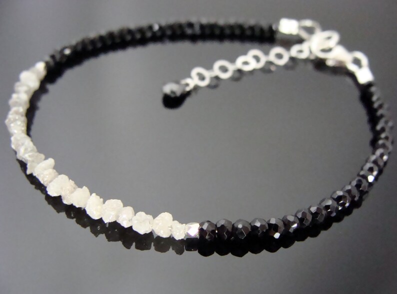 May include: A silver chain bracelet with black and white beads. The bracelet has a silver clasp and is made with rough cut stones.