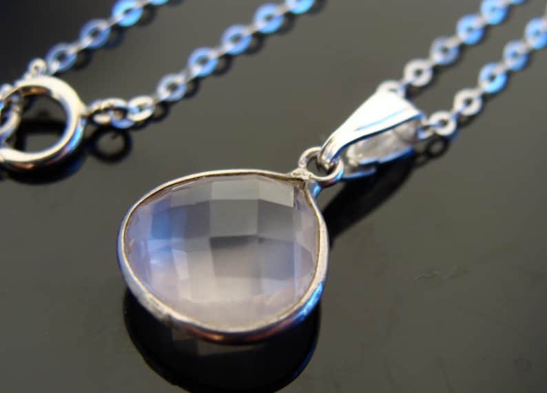May include: A silver chain necklace with a teardrop-shaped pendant featuring a clear, faceted, pale pink gemstone.