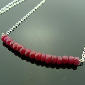 Op de afbeelding: Een zilveren ketting met een rij rode robijn kralen.