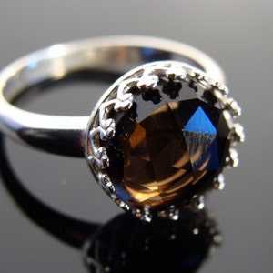 Puede incluir: Un anillo de plata con una gran piedra preciosa marr&oacute;n facetada engastada en un engaste decorativo de plata en forma de corona.