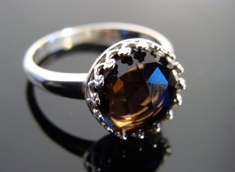 Puede incluir: Un anillo de plata con una gran piedra preciosa marr&oacute;n facetada engastada en un engaste decorativo de plata en forma de corona.