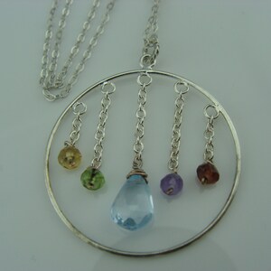 May include: A silver necklace with a circular pendant featuring five dangling gemstones. The gemstones are blue, green, yellow, purple, and red.
