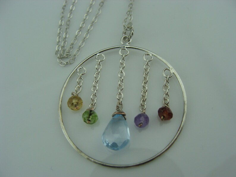 May include: A silver necklace with a circular pendant featuring five dangling gemstones. The gemstones are blue, green, yellow, purple, and red.