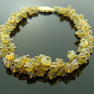 May include: A gold-toned bracelet featuring clusters of yellow-green gemstones. The bracelet is made of delicate gold chains and small gold beads. The gemstones have a translucent quality, and the bracelet is displayed on a reflective surface.