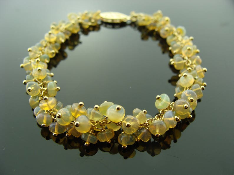 May include: A gold-toned bracelet featuring clusters of yellow-green gemstones. The bracelet is made of delicate gold chains and small gold beads. The gemstones have a translucent quality, and the bracelet is displayed on a reflective surface.