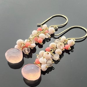 May include: A pair of dangle earrings with pink and coral beads and a large pink gemstone at the bottom of each earring.